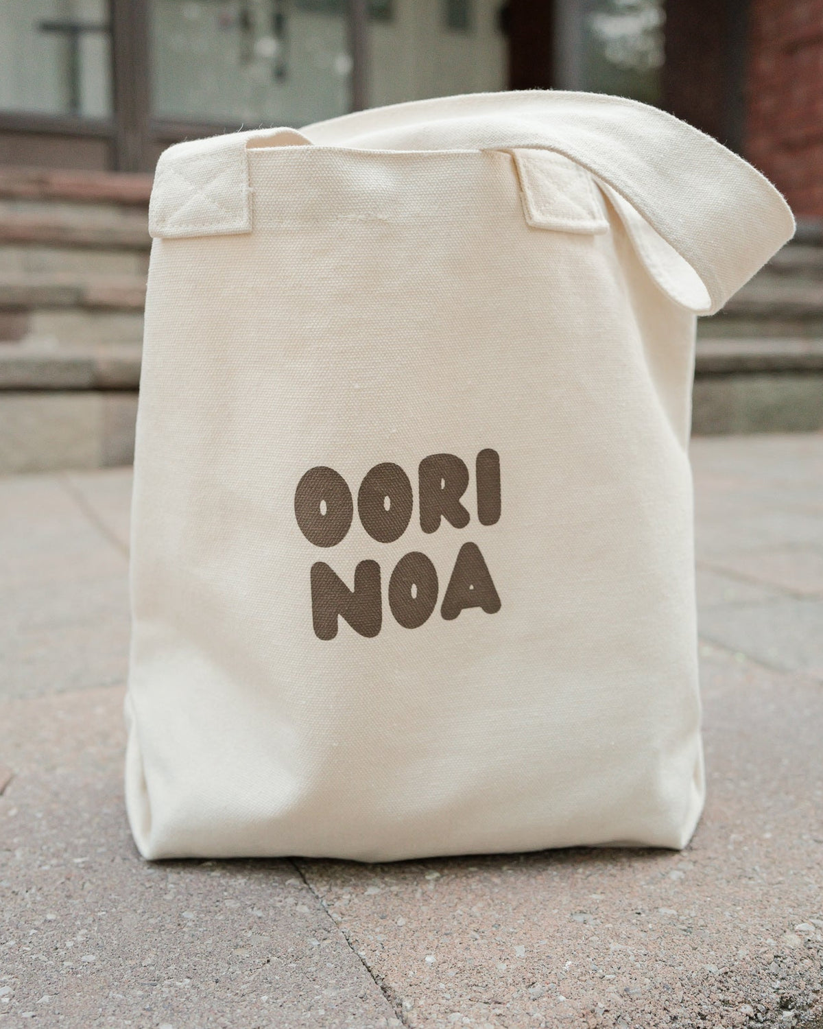Beige tote bag with 'Oori Noa' text on a stone surface